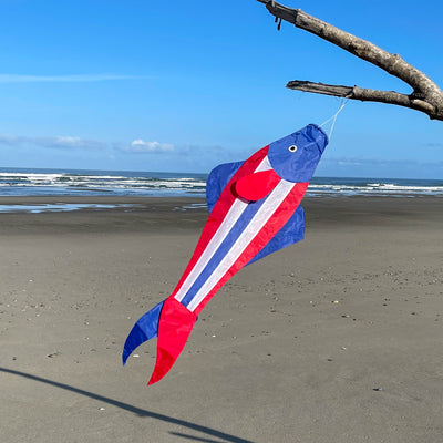 Patriot Trout 48" Fishsock in vibrant red, white, and blue swaying in the breeze from a hanging point in a garden setting.