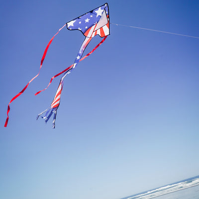 Patriotic 30-inch Mini Fly-Hi kite displaying bright stars and stripes design flying in the sky with attached 60-inch streamer tails.