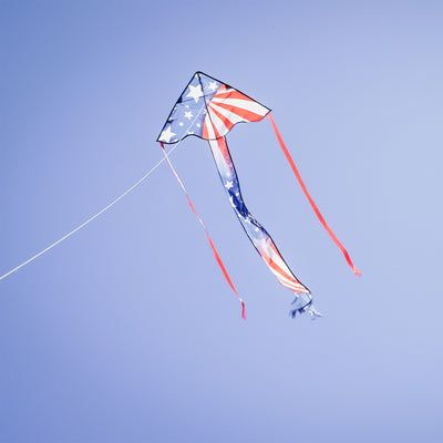 Patriotic 30-inch Mini Fly-Hi kite displaying bright stars and stripes design flying in the sky with attached 60-inch streamer tails.