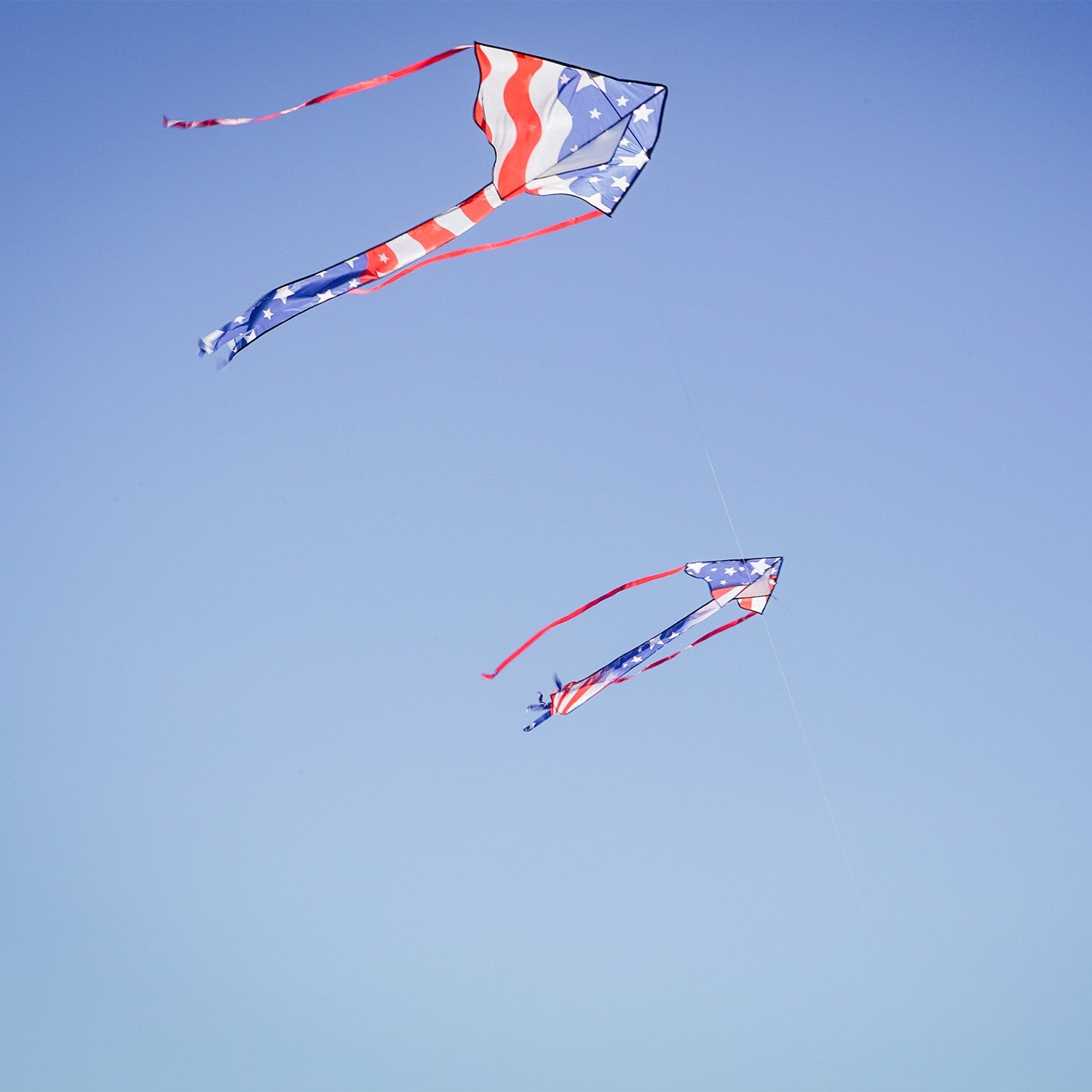 Patriotic 30-inch Mini Fly-Hi kite displaying bright stars and stripes design flying in the sky with attached 60-inch streamer tails.