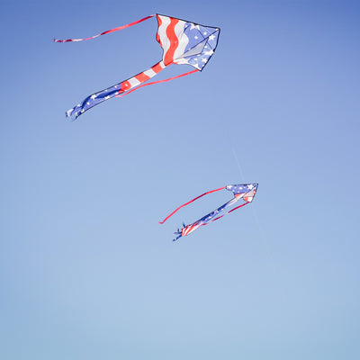 Patriotic 30-inch Mini Fly-Hi kite displaying bright stars and stripes design flying in the sky with attached 60-inch streamer tails.