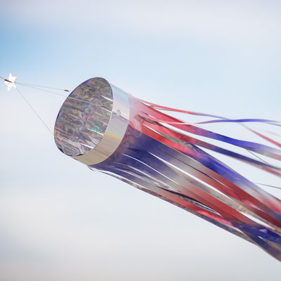 Patriotic 51 inch Mylar windsock in red, white, and blue, shimmering in sunlight while fluttering in the breeze, perfect for festive outdoor decoration.