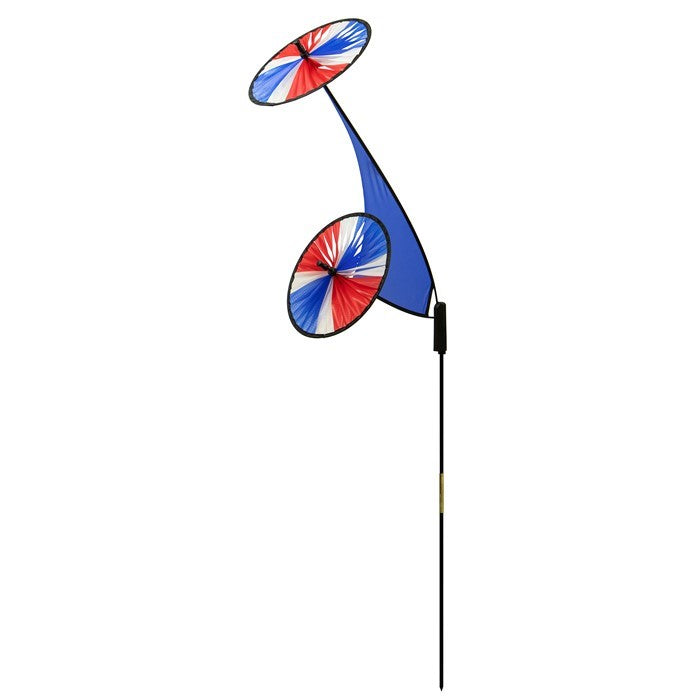 Patriotic Space Flower Ground Spinner with red, blue, and white wheels swaying in the wind, displayed in a lush garden setting.