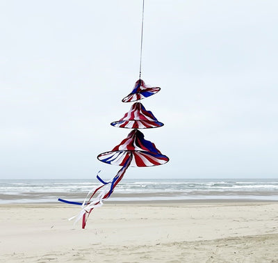 Patriotic Triple Jelly wind decoration featuring three spinning structures in red, white, and blue colors, hanging outdoors in a garden setting.