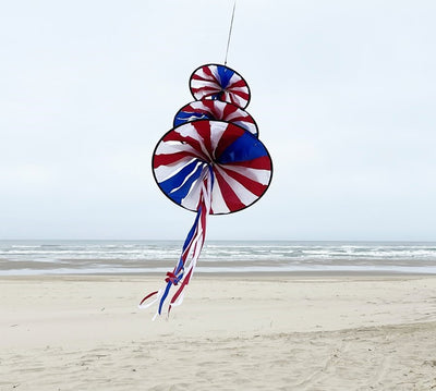 Patriotic Triple Jelly wind decoration featuring three spinning structures in red, white, and blue colors, hanging outdoors in a garden setting.