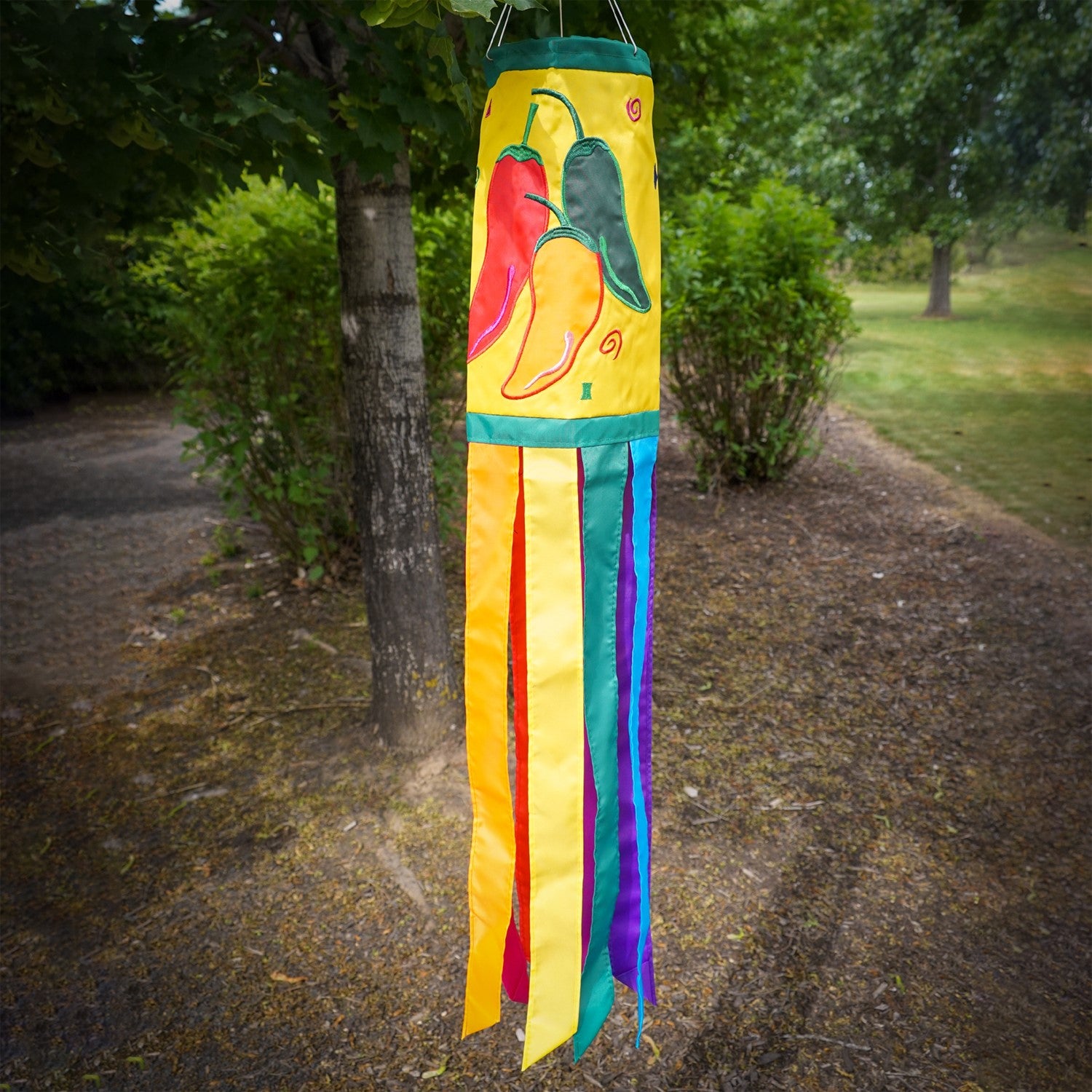 A colorful Pepper Fiesta 40" windsock featuring cheerful chili peppers and fluttering tails hanging gracefully in an outdoor garden setting.