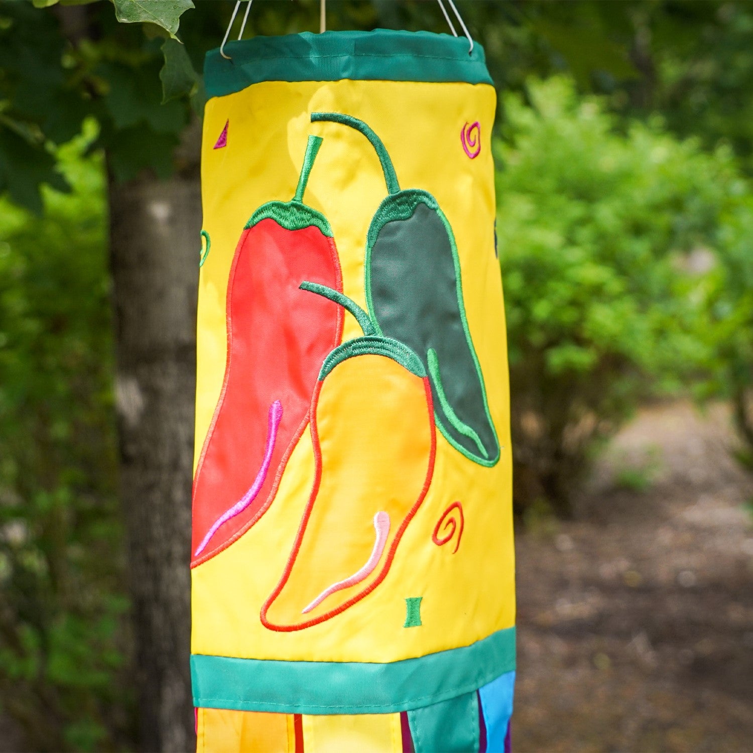 A colorful Pepper Fiesta 40" windsock featuring cheerful chili peppers and fluttering tails hanging gracefully in an outdoor garden setting.