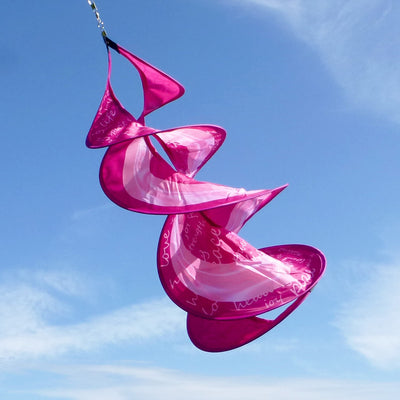 A Pink Ribbon Spin Duet hanging in a garden, featuring vibrant pink ribbon graphics and a spinning mechanism, symbolizing breast cancer awareness.