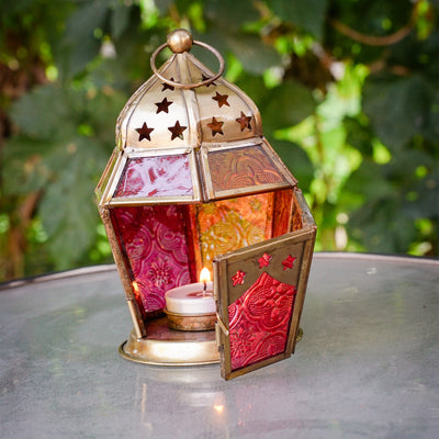 Pink and yellow hex glass tealight lantern with stamped designs and metal frame, elegantly displaying a tealight candle in a cozy setup.