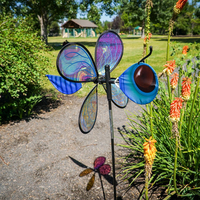 Pivoting Dragonfly Bug Spinner featuring iridescent Mylar wings and a fiberglass frame, elegantly displayed in a vibrant garden setting.