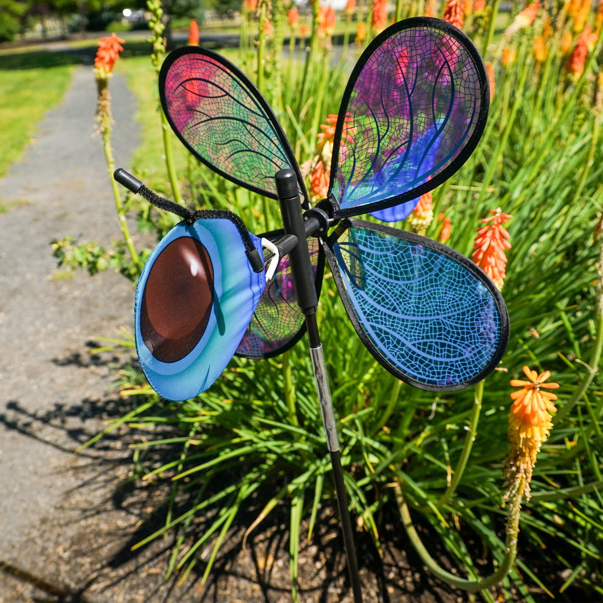 Pivoting Dragonfly Bug Spinner featuring iridescent Mylar wings and a fiberglass frame, elegantly displayed in a vibrant garden setting.