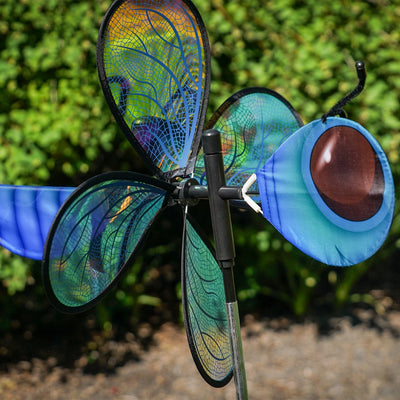 Pivoting Dragonfly Bug Spinner featuring iridescent Mylar wings and a fiberglass frame, elegantly displayed in a vibrant garden setting.
