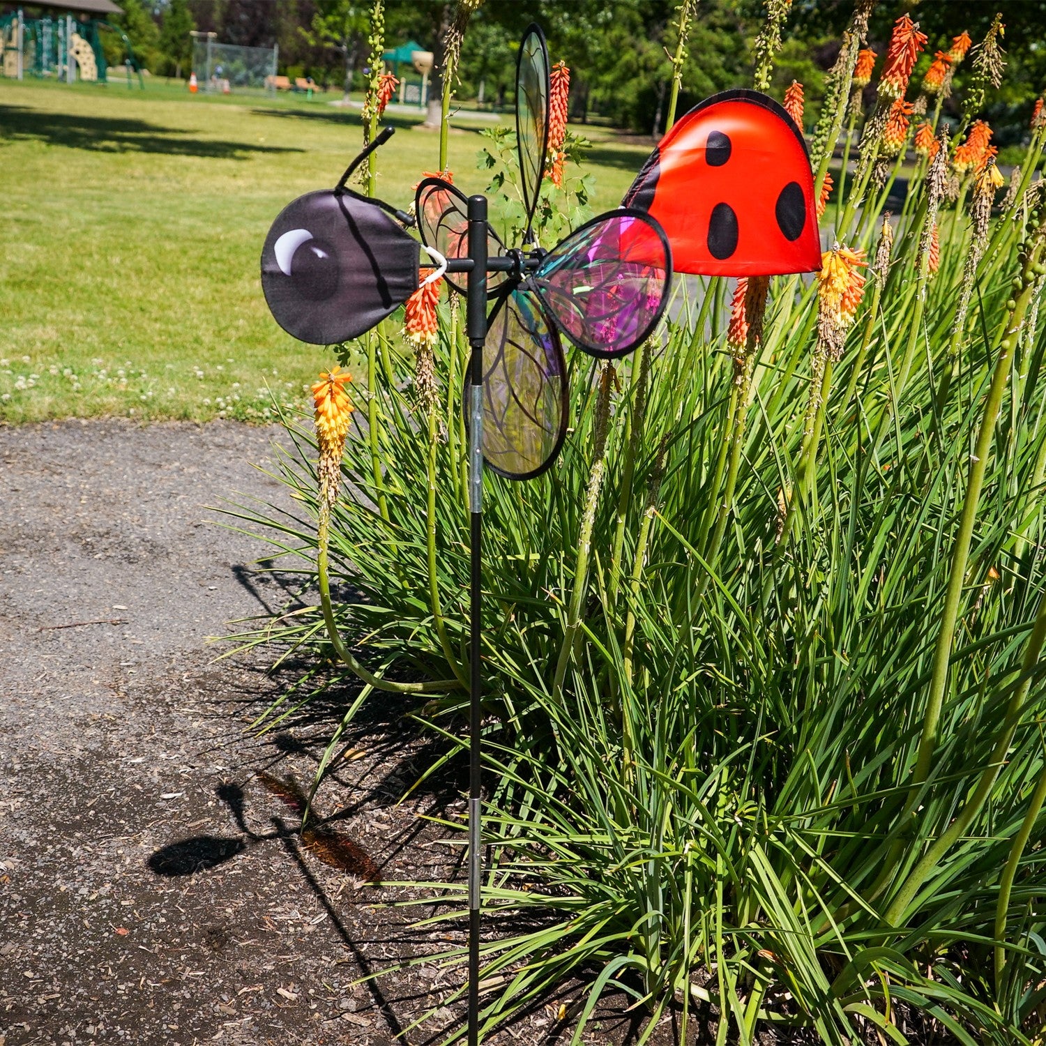 Pivoting Ladybug Spinner with vibrant design and iridescent petals spinning in a sunny garden setting, mounted on a sturdy pole.