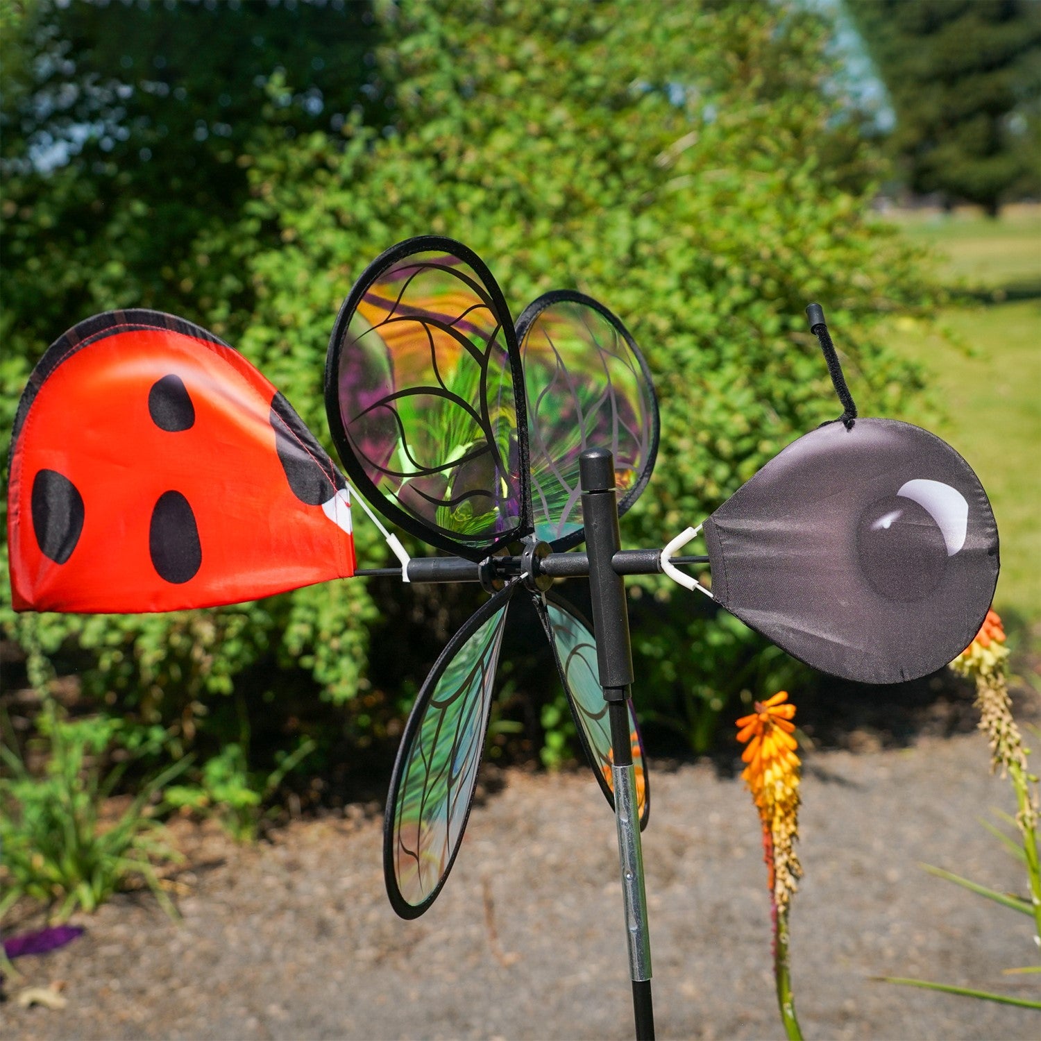 Pivoting Ladybug Spinner with vibrant design and iridescent petals spinning in a sunny garden setting, mounted on a sturdy pole.