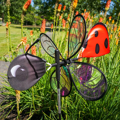 Pivoting Ladybug Spinner with vibrant design and iridescent petals spinning in a sunny garden setting, mounted on a sturdy pole.