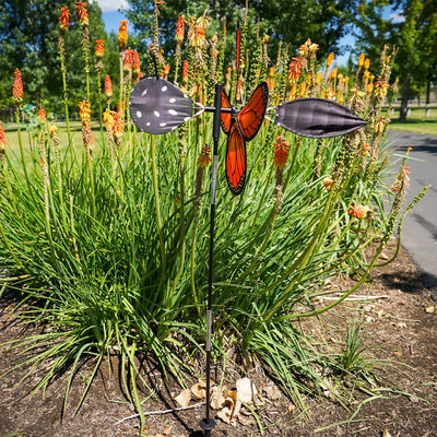 Vibrant Pivoting Monarch Butterfly Spinner in a garden, showcasing colorful petal design and fiberglass frame, adding motion to the outdoor space.