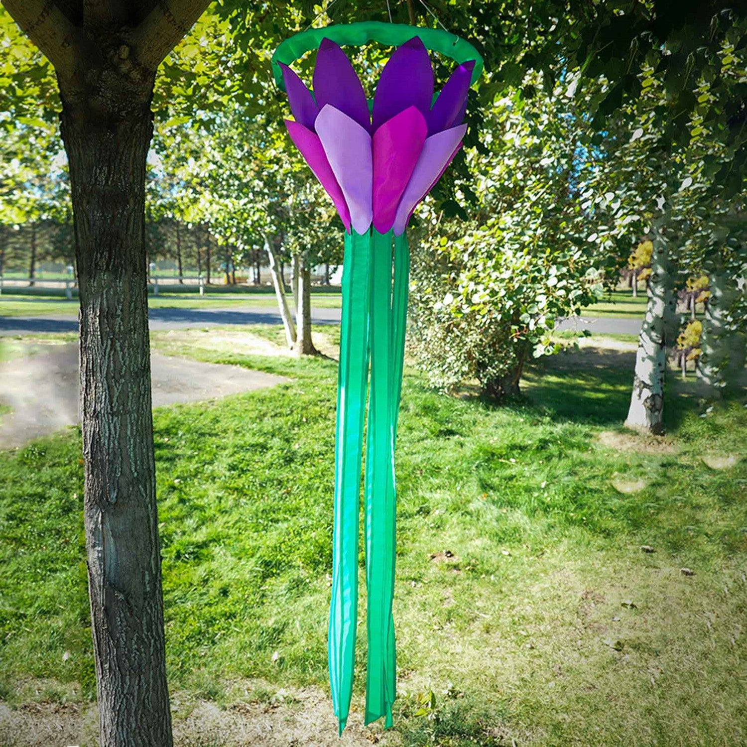 Purple 38 inch lotus flower windsock with bright petals and flowing green tails, elegantly displayed in a garden setting, showcasing its colorful design.
