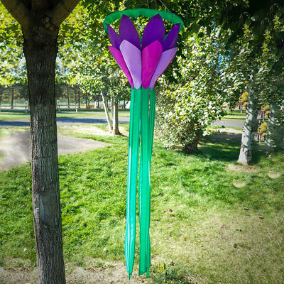 Purple 38 inch lotus flower windsock with bright petals and flowing green tails, elegantly displayed in a garden setting, showcasing its colorful design.
