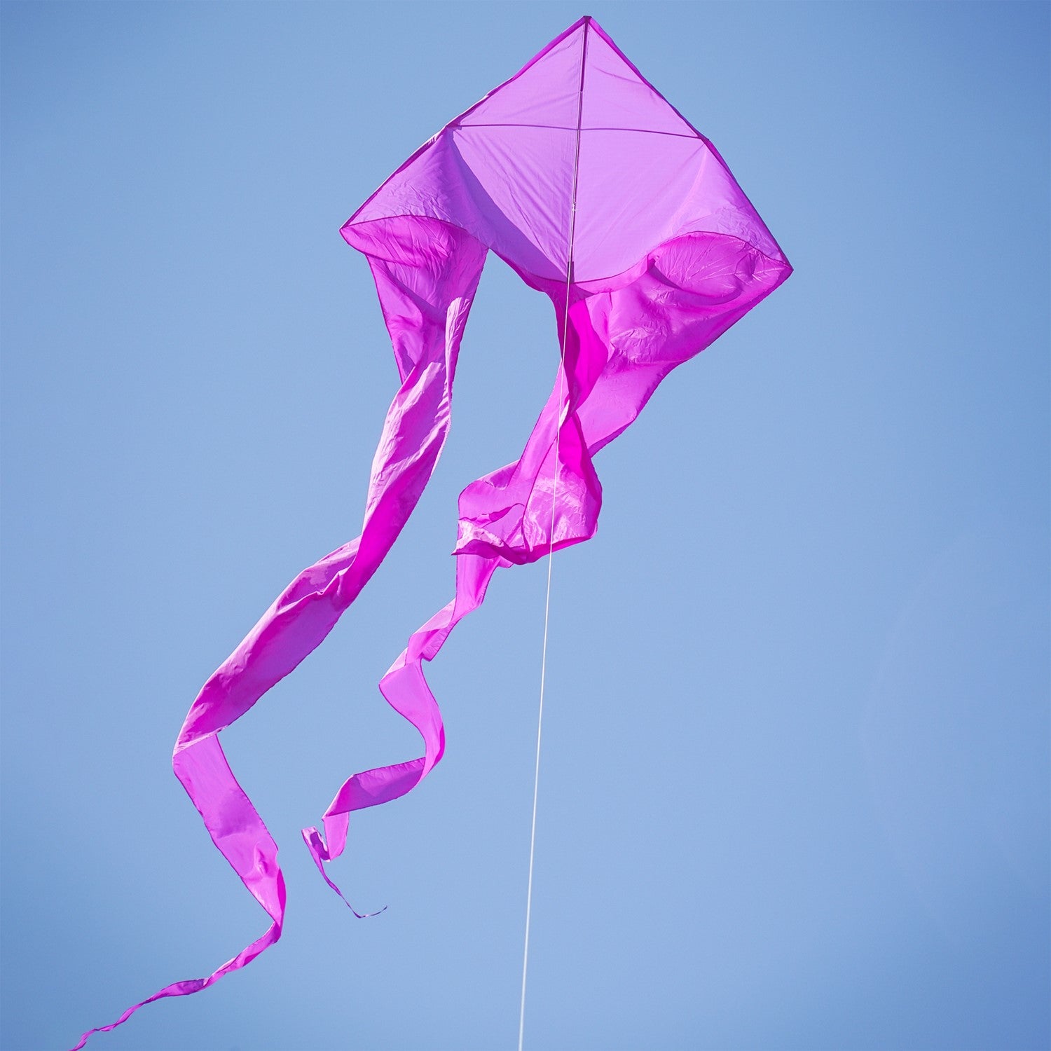Purple 77' Wave Delta Kite soaring in a bright blue sky with long flowing tails dancing behind it, designed for easy flying.