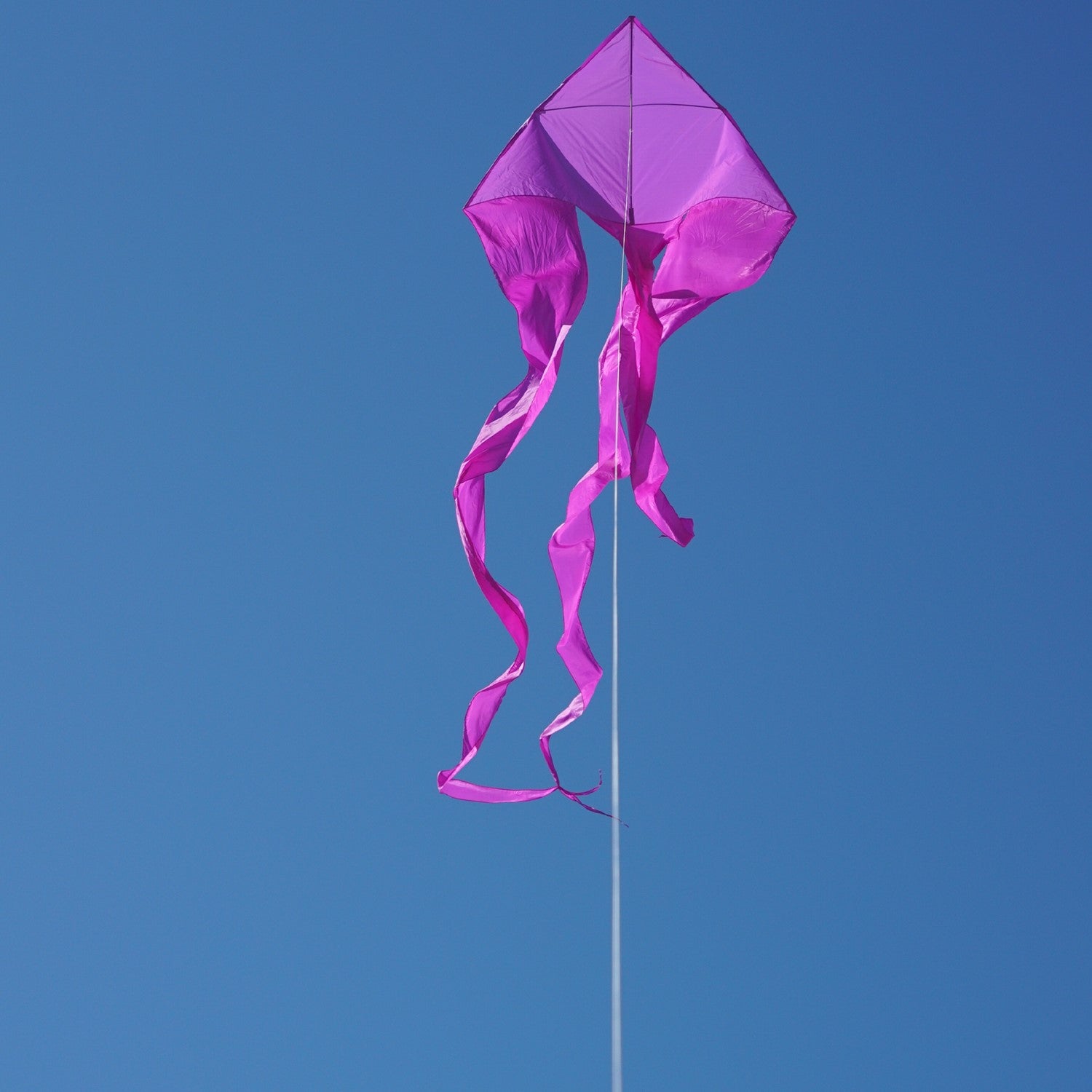 Purple 77' Wave Delta Kite soaring in a bright blue sky with long flowing tails dancing behind it, designed for easy flying.