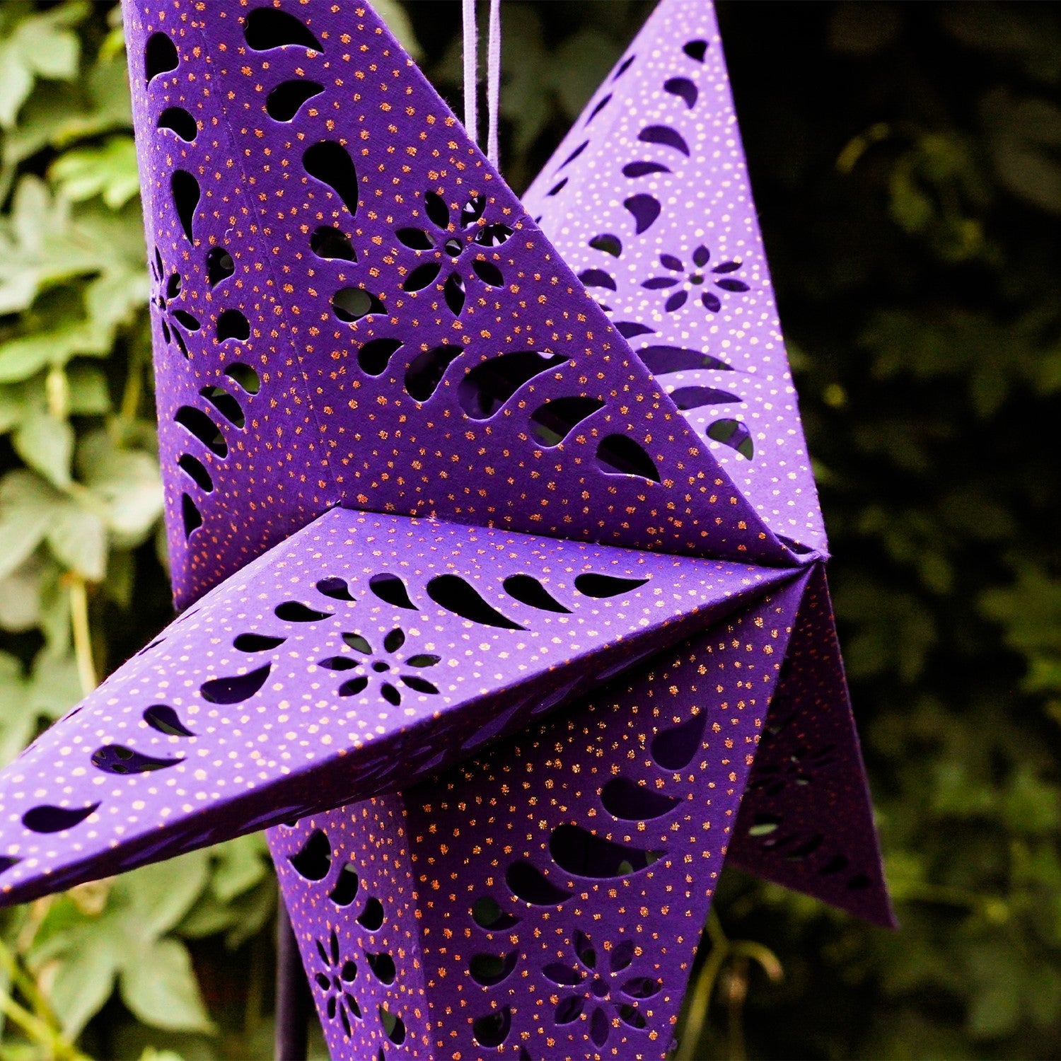Purple Paper Star Lantern with intricate cutouts and gold accents, hanging indoors, illuminated with fairy lights for a cozy glow.