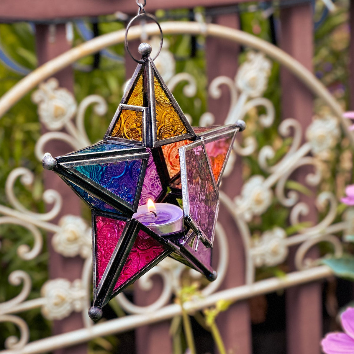 Rainbow 5-Point Star Hanging Tealight Lantern with multicolored glass panels and metal frame, displayed outdoors, radiating warm light from a tealight candle.