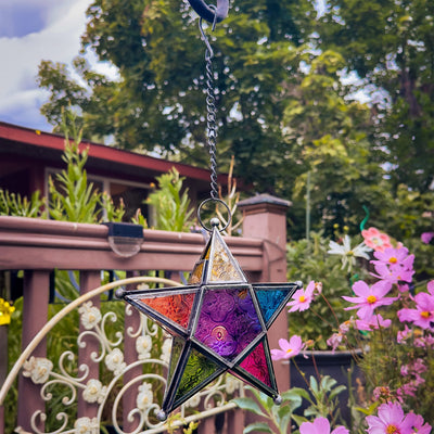 Rainbow 5-Point Star Hanging Tealight Lantern with multicolored glass panels and metal frame, displayed outdoors, radiating warm light from a tealight candle.