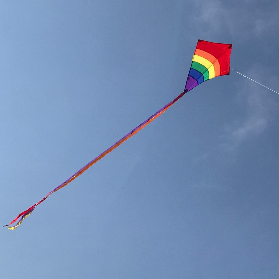 Rainbow Arch 27-Inch Diamond Kite displaying colorful arcs in the sky, ready for flying on a bright day outdoors.