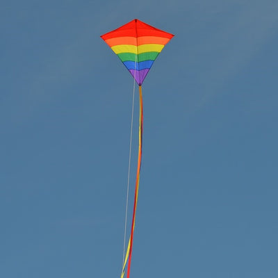 Rainbow Arch 39-Inch Diamond Kite in vibrant colors, featuring long fabric tails, soaring against a bright blue sky on a sunny day.