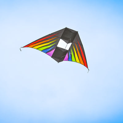 Rainbow Burst 6' Conyne Delta Kite featuring vibrant colors displayed in an outdoor setting with blue skies and fluffy clouds, ideal for family fun.