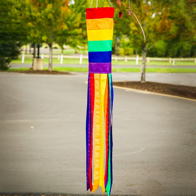 Rainbow Column 40\" windsock featuring bright colors and 12 coordinating tails, hanging in a garden setting on a sunny day.