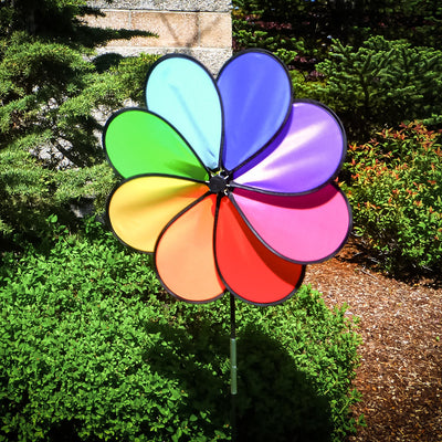 Rainbow Dazy Petal Spinner features eight colorful petals arranged in a flower design, spinning in the breeze atop a sturdy pole in a garden setting.