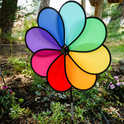 Rainbow Dazy Petal Spinner features eight colorful petals arranged in a flower design, spinning in the breeze atop a sturdy pole in a garden setting.