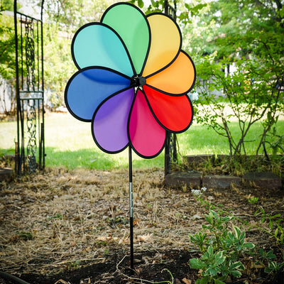 Rainbow Dazy Petal Spinner features eight colorful petals arranged in a flower design, spinning in the breeze atop a sturdy pole in a garden setting.