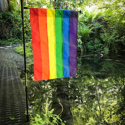 Vibrant Rainbow Garden Flag featuring bright colors displayed on both sides, set against a garden backdrop with flowers.
