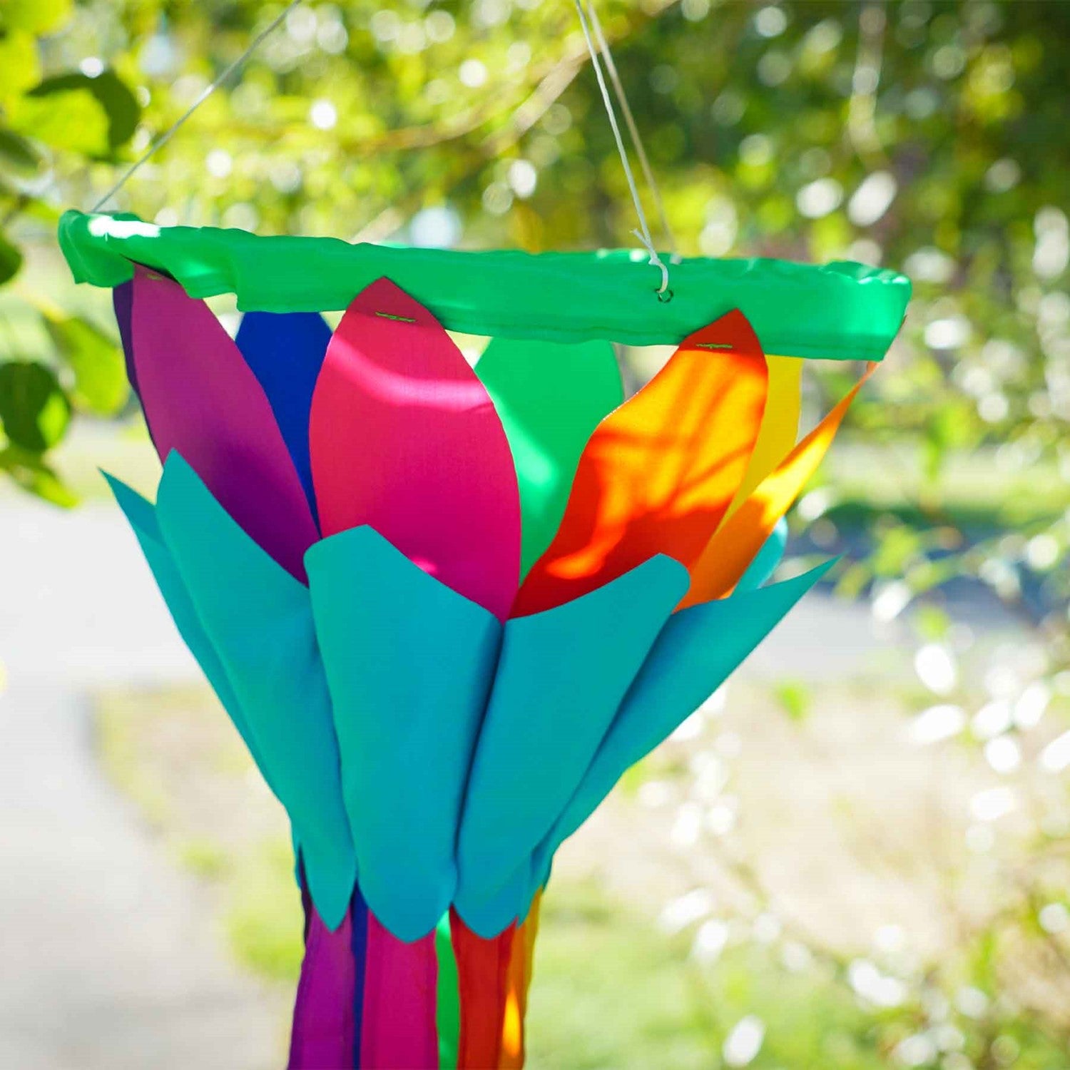 Rainbow 38'' Lotus Flower Windsock with colorful petals and flowing tails, gently swaying in the breeze, hanging in a garden setting.
