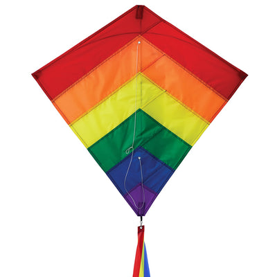 Rainbow Overlay 30-inch Diamond Kite flying in the blue sky with colorful streamer tails trailing below, showcasing its vibrant design.