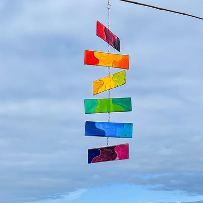 Rainbow Resin Mobile with six colorful translucent blocks hanging outdoors, catching sunlight and swaying gently in the breeze.