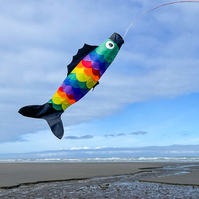 Rainbow Scales Fishsock, a colorful and whimsical windsock with detailed applique, displayed in an outdoor garden setting, showcasing its design.