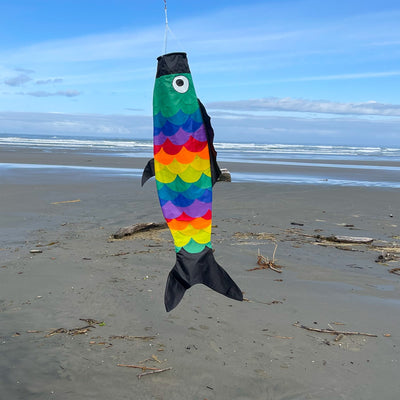 Rainbow Scales Fishsock, a colorful and whimsical windsock with detailed applique, displayed in an outdoor garden setting, showcasing its design.