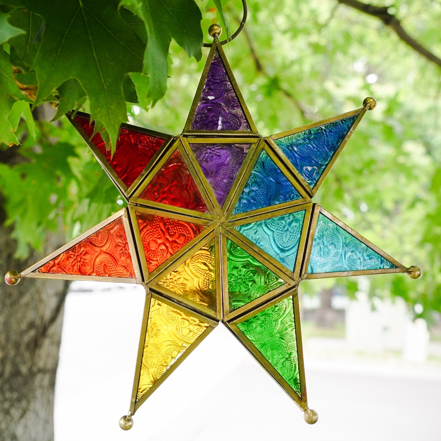 Vibrant Rainbow Seven Point Star Tealight Lantern hanging outdoors, showcasing intricate glass panels and golden metal framing.