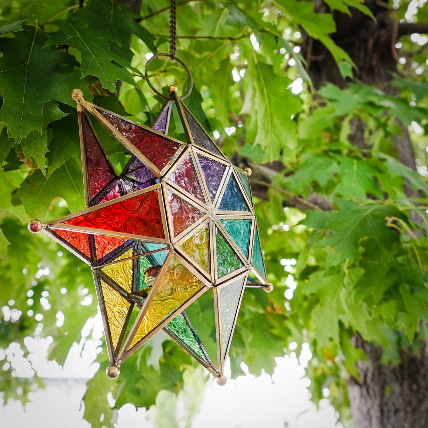 Vibrant Rainbow Seven Point Star Tealight Lantern hanging outdoors, showcasing intricate glass panels and golden metal framing.