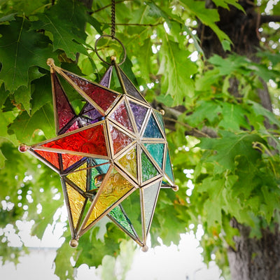 Vibrant Rainbow Seven Point Star Tealight Lantern hanging outdoors, showcasing intricate glass panels and golden metal framing.