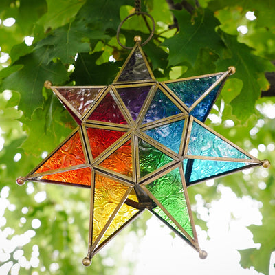 Vibrant Rainbow Seven Point Star Tealight Lantern hanging outdoors, showcasing intricate glass panels and golden metal framing.