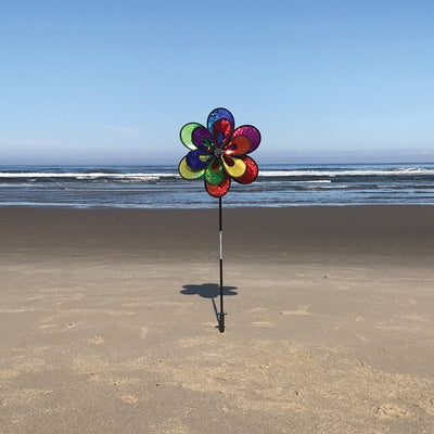 Rainbow Sparkle Windee Wheelz and Flower Spinner featuring double Mylar wheels adorned with colorful petals, spinning in a gentle breeze in a garden setting.