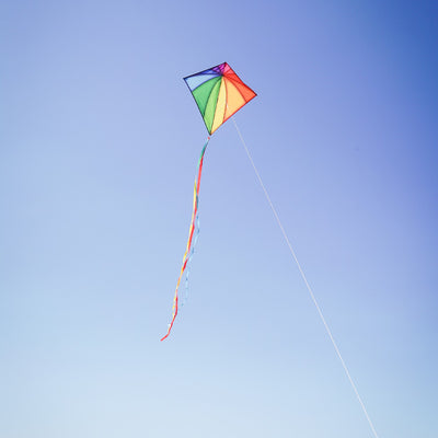 Colorful Rainbow Stained Glass 30-inch Diamond Kite flying against a blue sky, showcasing its vibrant stained glass patterns and attached tails.