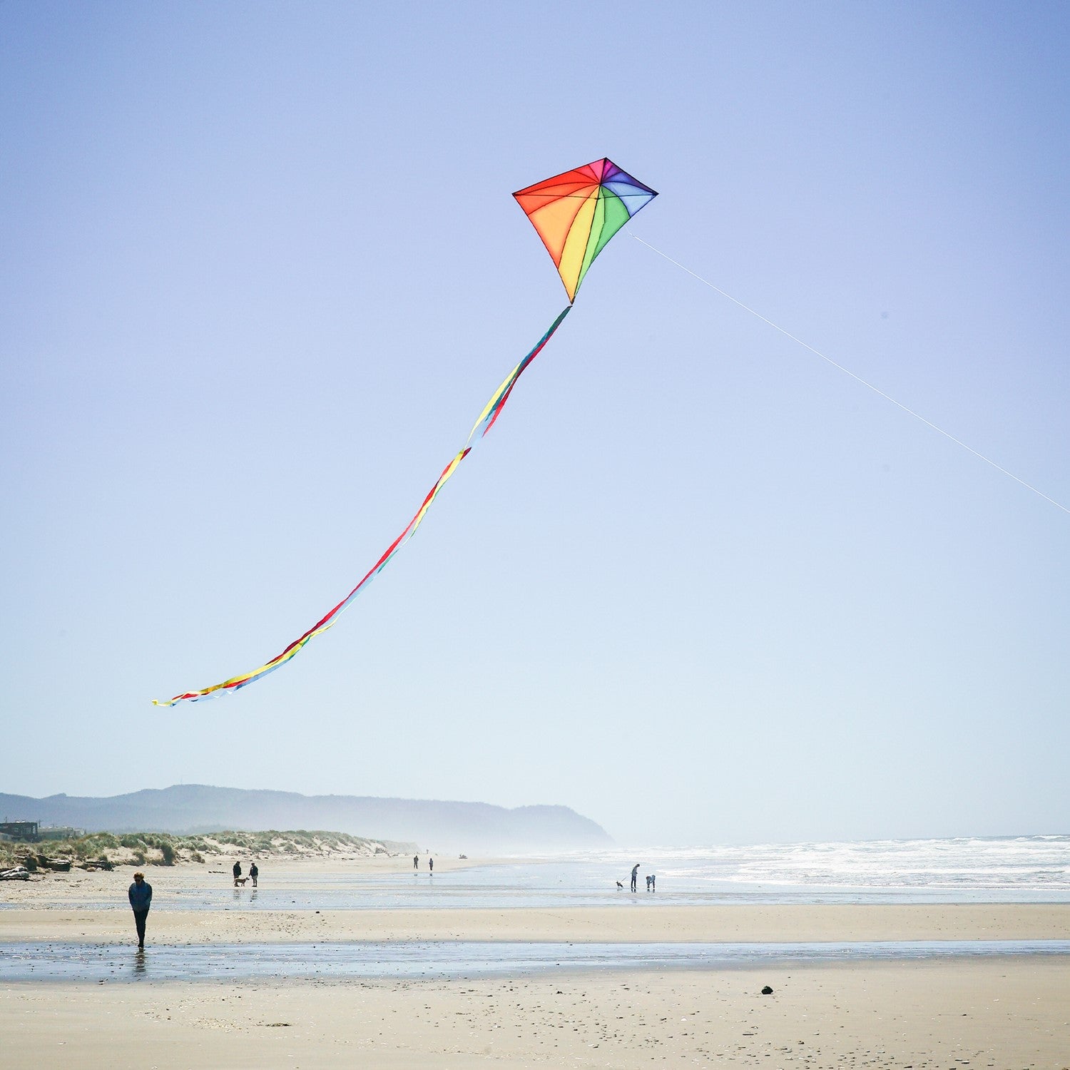 Rainbow Stained Glass 46" Diamond Kite soaring against a blue sky, showcasing vibrant colors and long, flowing tails during flight.