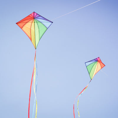 Rainbow Stained Glass 46" Diamond Kite soaring against a blue sky, showcasing vibrant colors and long, flowing tails during flight.