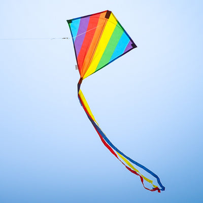 Rainbow Stripe 18" Diamond Kite flying high against a blue sky with colorful tails trailing behind, showcasing its vibrant spectrum design and classic shape.