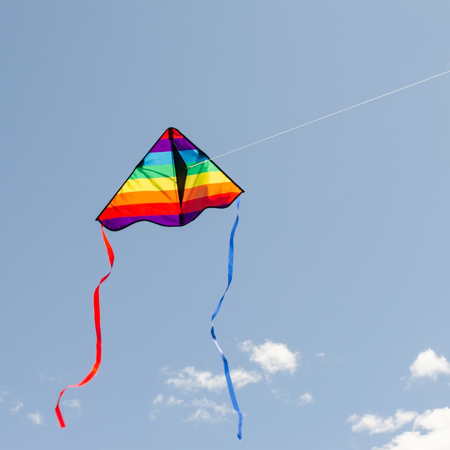 Colorful Rainbow Stripe 30-inch Delta Kite, featuring durable ripstop fabric and stable design, displayed soaring in a bright blue sky with playful tails fluttering below.